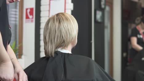 junge frau, die ihre haare im friseursalon anzieht. friseur-stylist bei der arbeit. mann friseur, der haare im schönheitssalon bürstet