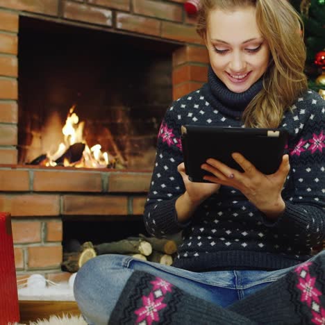 Una-Mujer-Joven-Usa-Una-Tableta-En-El-árbol-De-Navidad-Y-La-Chimenea-1