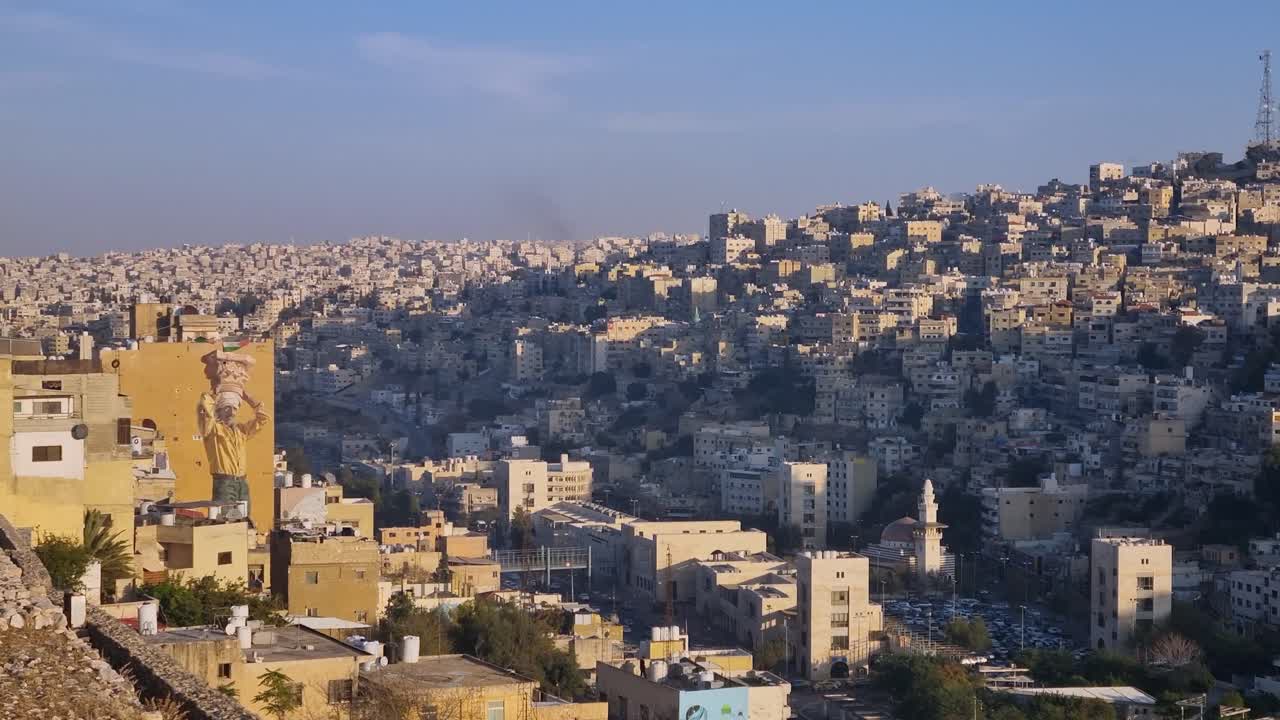 Ampio panorama del tramonto su Amman, in Giordania, con gli ultimi raggi di sole che illuminano il quartiere collinare di Jabal al-Taj, mettendo in risalto le case in pietra a più livelli e la densità urbana