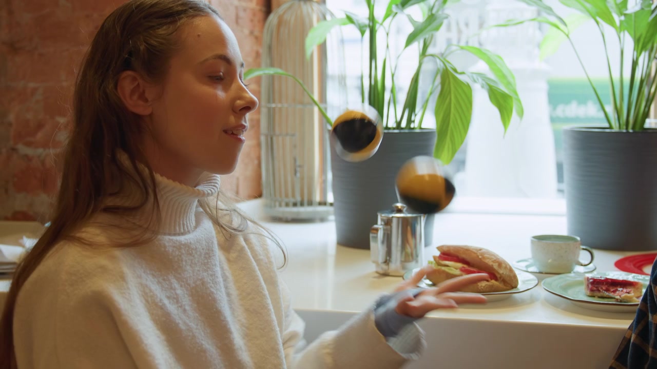 Close up of young woman and man sitting at table in indoor cafe interacting with small black yellow balls. scene includes food items like sandwiches cake cups on white countertop potted