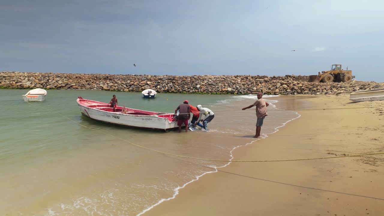 Men putting Motor on Fishing motor boat moored in shallow water beach to go fishing. Daily Teamwork handmade, tropical coast la Guaira Venezuela