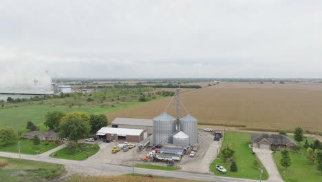 grain silos, barns, and a natural gas power plant by a cooling pond in the countryside, aerial