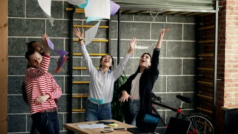 colegas de negocios multiétnicos se divierten bailando en oficinas modernas lanzando documentos de papel y celebrando el éxito del proyecto