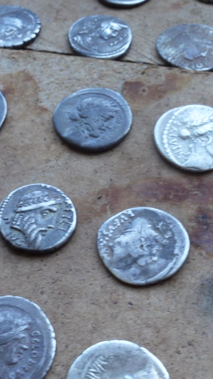 Vista vertical de monedas romanas de plata de varios emperadores sobre una mesa de madera antigua