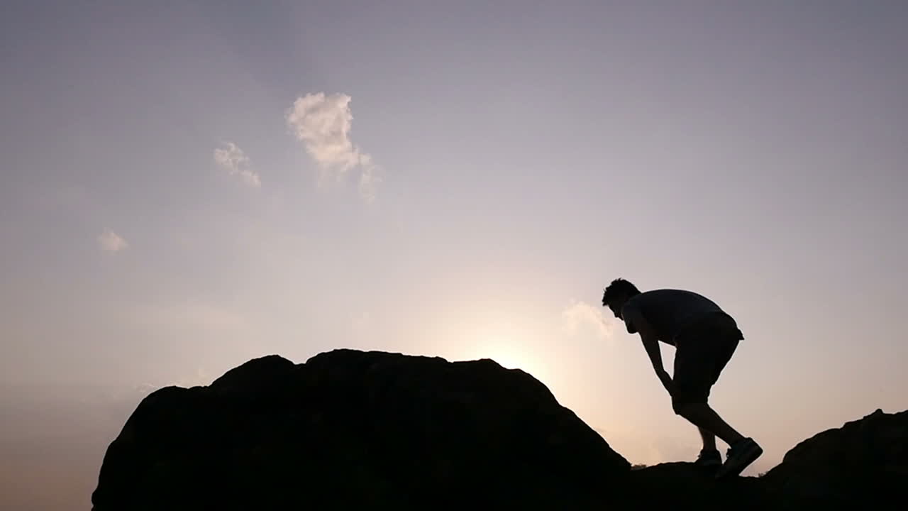 Silhouette of a Person Climbing a Rock at Sunrise/Sunset
