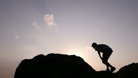 silhouette of a person climbing a rock at sunrise/sunset