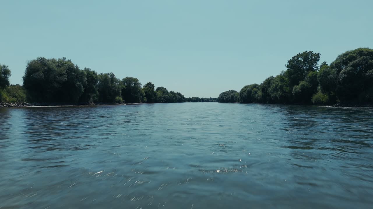 calm river stretches through forested banks with blue sky overhead