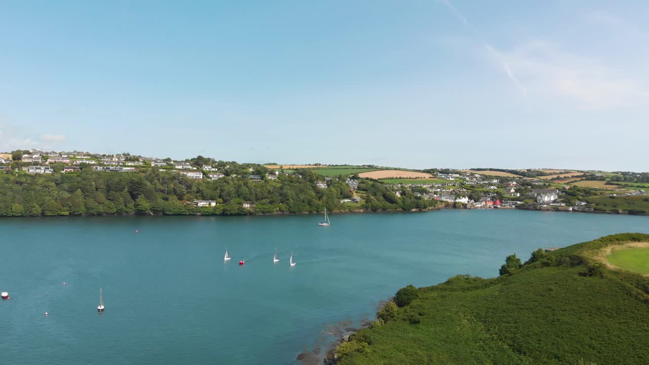 Gorgeous blue green waters form the entrance to this idyllic harbor scene as sailing boats enter and leave , some yachts lie peacefully at anchor
