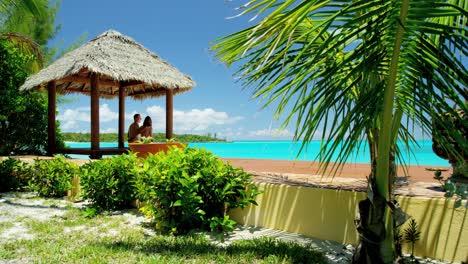 una pareja sentada en una cabaña de tiki con techo de paja en la playa