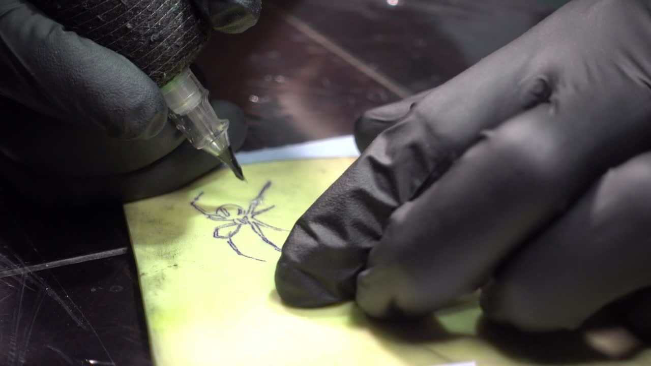 un artista del tatuaje dibujando una araña negra en la piel