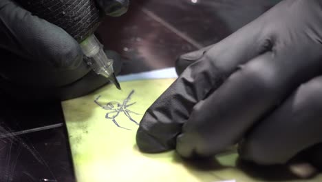 a tattoo artist drawing a black spider on skin