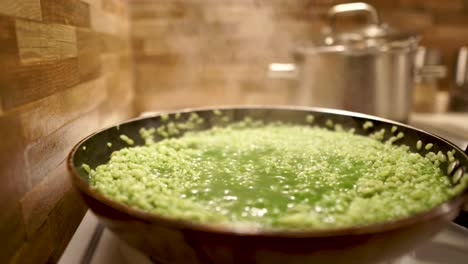 liquid bubbling away in a green spinach risotto cooking on the stove, pan right, 4k