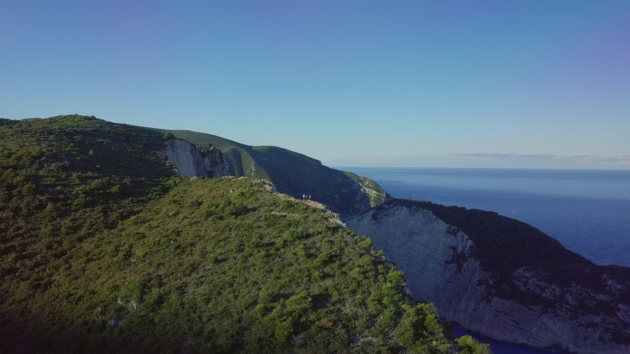 Drone che sorvola persone su una scogliera per svelare la spiaggia del relitto di Navagio all'alba.