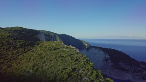 Antenne,-Die-Sich-über-Menschen-Auf-Einer-Klippe-Bewegt,-Um-Den-Sonnenaufgang-Am-Strand-Von-Navagio-Shipwreck-Zu-Enthüllen