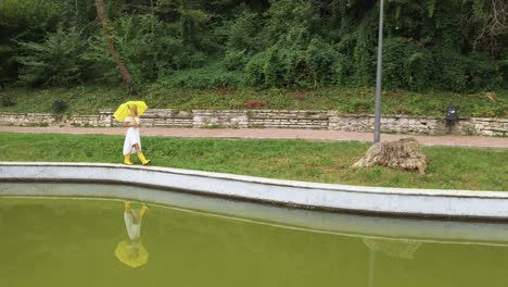 woman in white dress, umbrella walks near water reflection, aerial