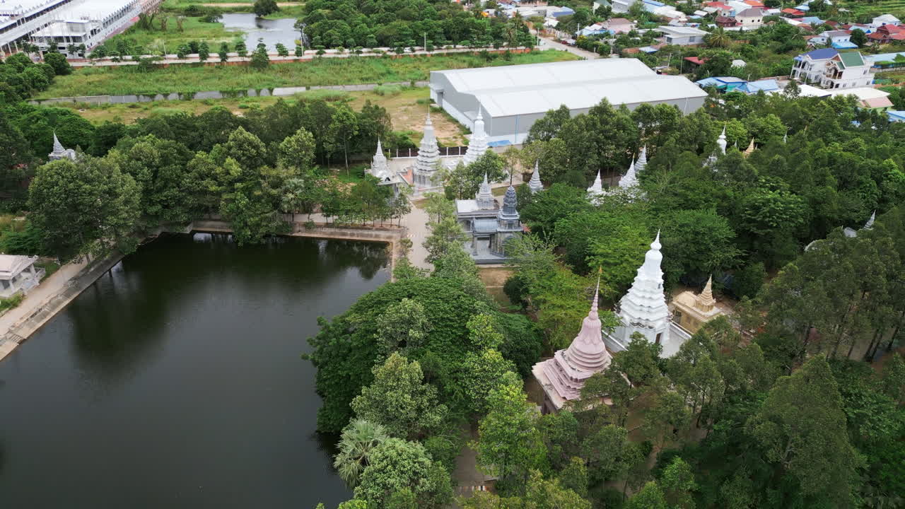 Aerial view of Cambodian temple grounds with white and pastel stupas surrounding a rectangular pond