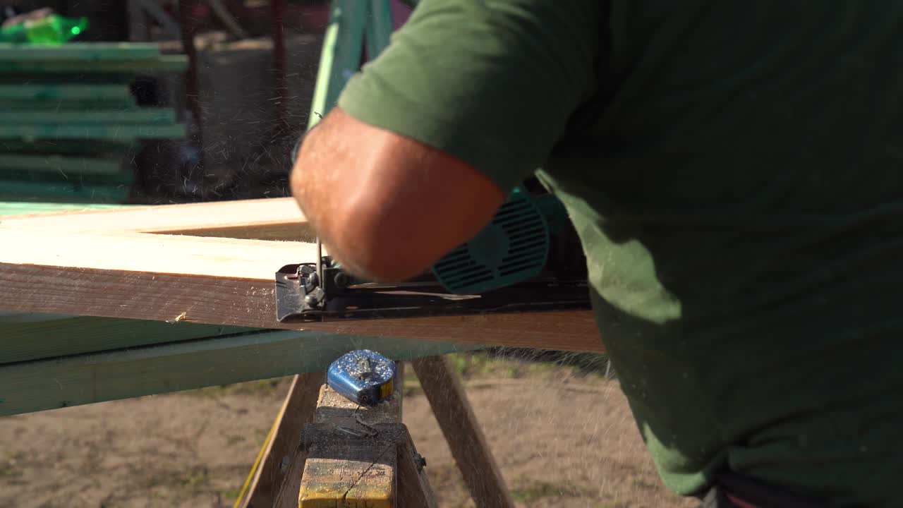 Carpenter uses electric saw to cut wooden beam on outdoor job site