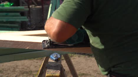 carpenter uses electric saw to cut wooden beam on outdoor job site
