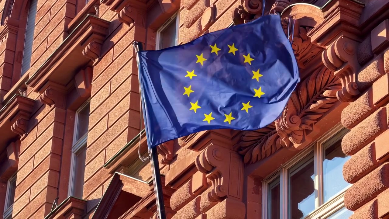 Primo piano della bandiera blu dell'UE con stelle gialle che sventola al vento sulla facciata di un edificio a Strasburgo, Francia.