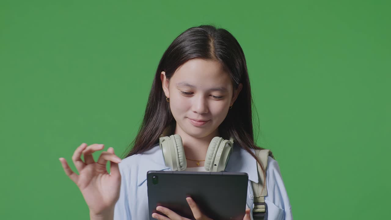 녹색 화면 배경 스튜디오에 서있는 동안 웃고 태블릿을 사용하는 배을 가진 아시아 십대 소녀 학생의 클로즈업