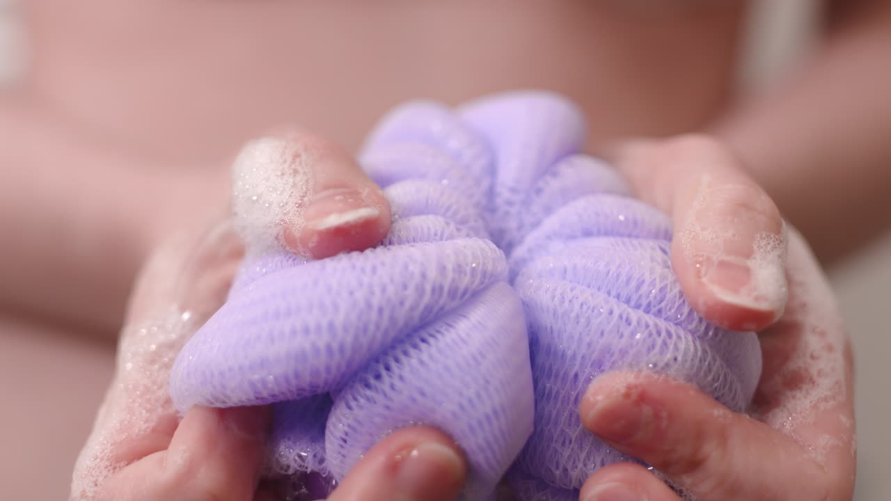 Purple loofah with soap in woman's hands, closeup