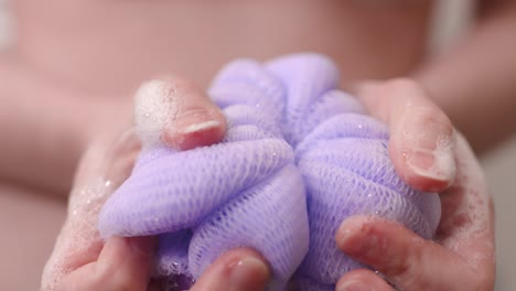 purple loofah with soap in woman's hands, closeup