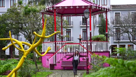 Female-tourist-poses-in-front-of-pink-kiosk-in-Jardim-Duque-da-Terceira