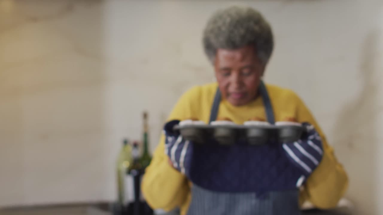 Vídeo de mulher afro-americana idosa feliz segurando e cheirando uma bandeja de cupcakes recém-assados