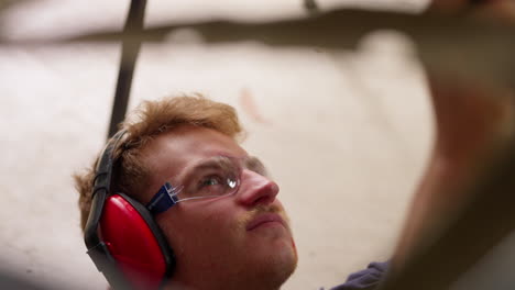 Caucasian-Man-With-Safety-Goggles-And-Ear-Muffs-Working-On-Project-In-Workshop,-4K-Close-Up