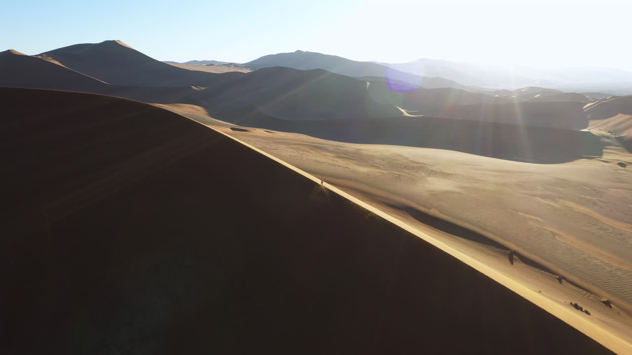 Drone shot following a person climbing on desert dunes, on a bright and sunny day