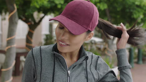 close up portrait of beautiful mixed race woman smiling happy looking at camera wearing hat standing on street in urban city background