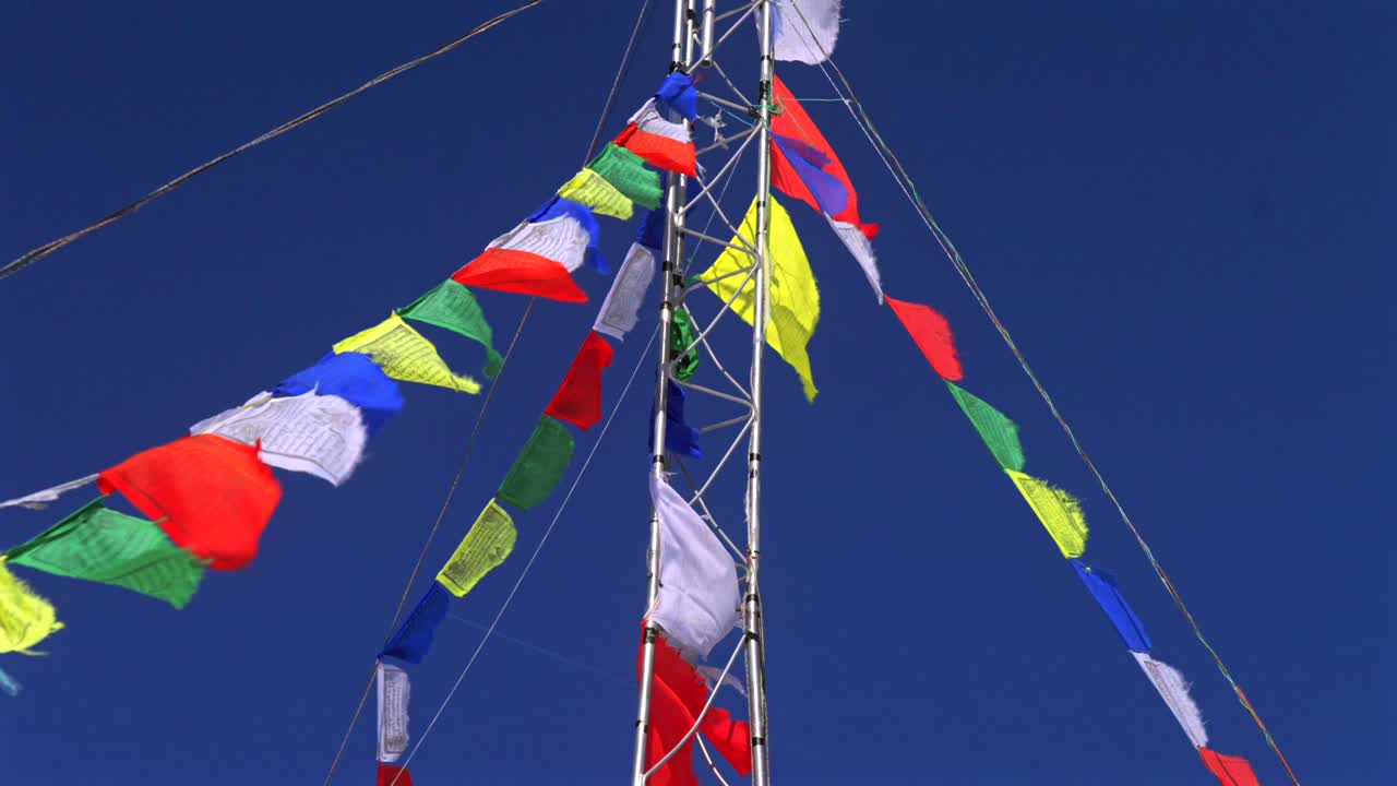 Aspen Highlands bowl blue bird sky sunny winter spring day Nepali prayer flags metal pole Colorado Snowmass Elk Mountains morning afternoon no clouds top of peak pan upwards motion