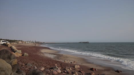 una playa con arena roja, negra y blanca y múltiples tipos de rocas con el muelle swakopmund en el fondo