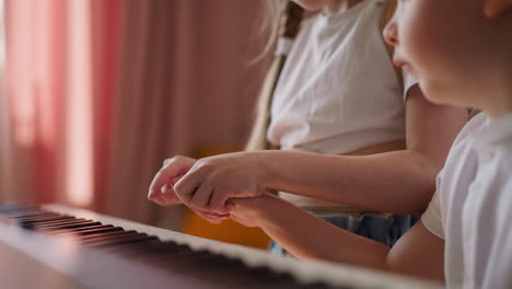 Little-girl-presses-piano-keys-with-brother-finger-at-home