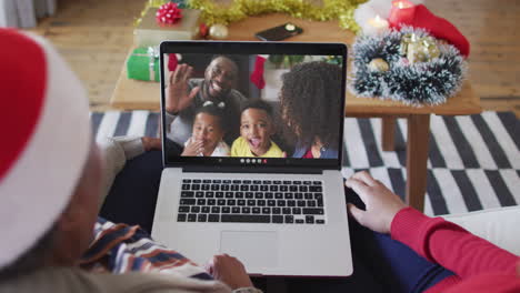 african american mother and daughter using laptop for christmas video call with family on screen