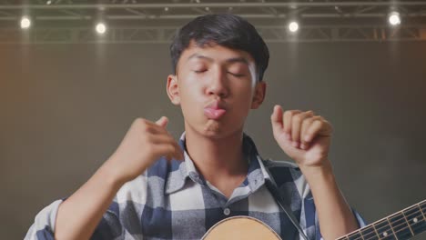 un primer plano de un adolescente asiático con una guitarra bailando en el escenario.