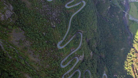 Aerial-top-down-view-of-tight-twisting-serpentine-road-as-it-winds-up-the-steep,-tree-covered-valley-side-of-a-Fjord-in-Norway