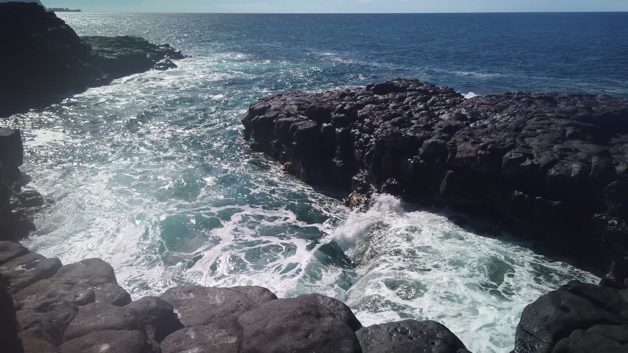Gimbal wide panning shot of seawater spilling into a tidepool among the ancient lava rocks near Queen's Bath on the Hawaiian island of Kaua'i