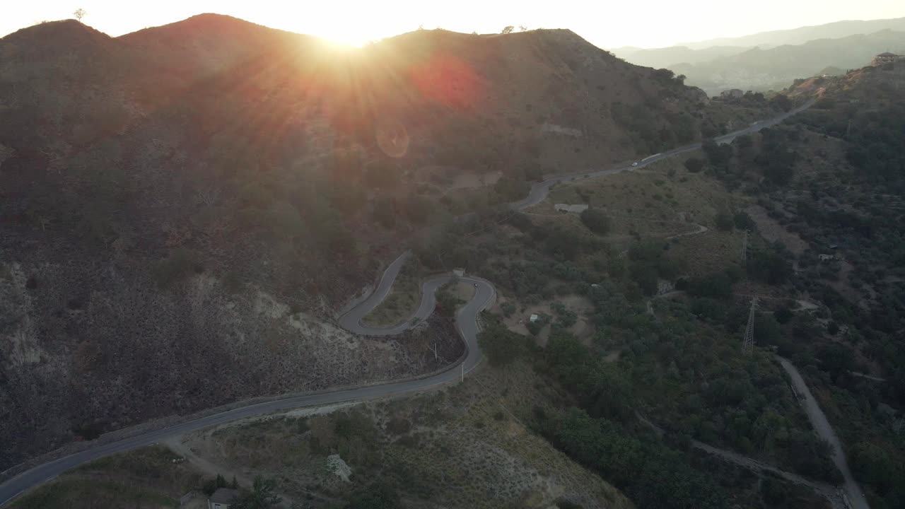 해가 지는 동안 이탈리아 남부의 휘어지는 산길을 가로질러 운전하는 차를 향해