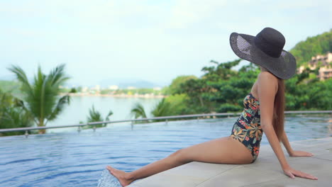 attractive rich asian woman in swimsuit sitting on poolsie on tropical holiday