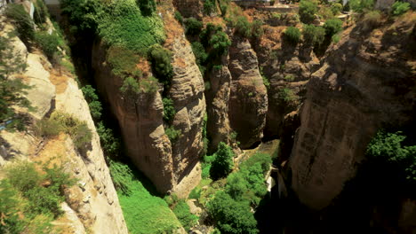 a dramatic aerial view of el tajo gorge in ronda, spain, showcasing steep rocky cliffs covered in greenery with a narrow river running through the bottom of the gorge