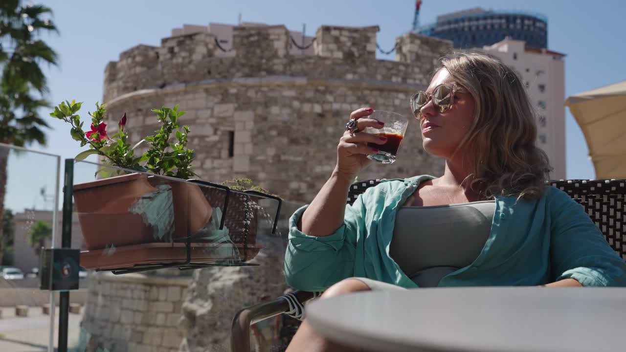 Bella donna si gode un drink su una terrazza cittadina al sole, rallentatore