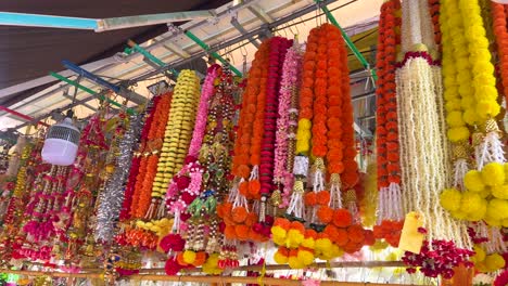 bright marigold and jasmine garlands hang densely in a vibrant market stall, illuminated by natural daylight, with a slow forward camera movement revealing intricate floral arrangements