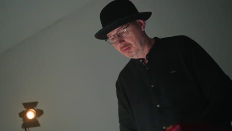 close-up of a keyboardist in a black outfit and hat playing a red sampler, set against a grey background