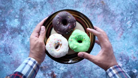 hand holding a plate of colorful donuts