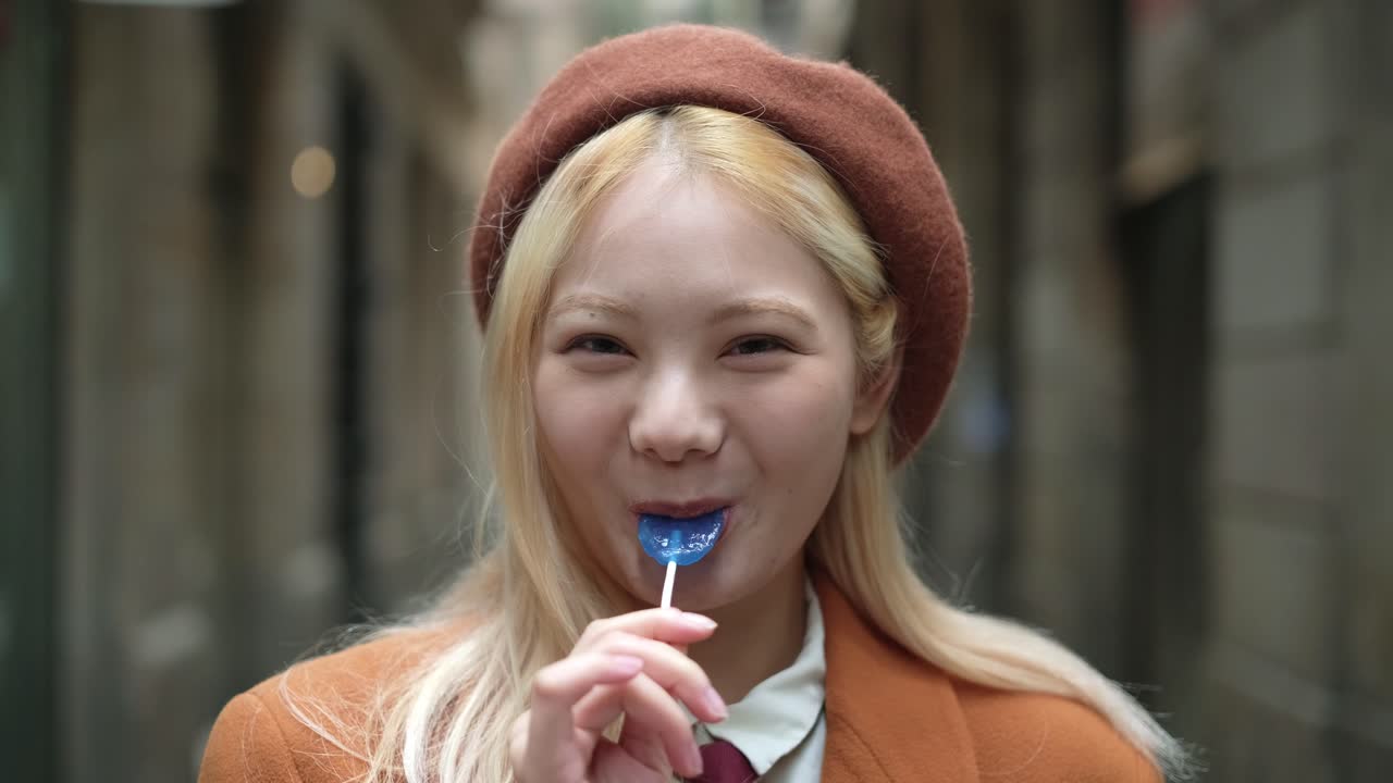 Woman with blond hair and beret holding a lollipop