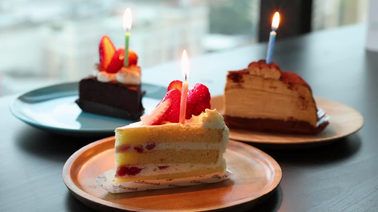 Three cakes with lit candles on plates, natural daylight, shallow depth, steady camera, celebratory mood
