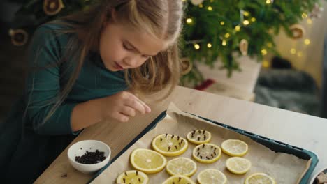 High-angle-view-of-caucasian-little-girl-preparing-dried-fruits-for-Christmas-decorations.