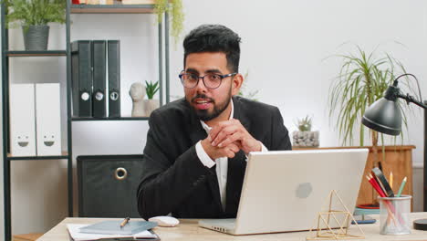 Hombre-De-Negocios-Trabajando-En-Una-Computadora-Portátil-Sonriendo-Amablemente-A-La-Cámara-Y-Saludando-Con-Las-Manos-En-La-Oficina