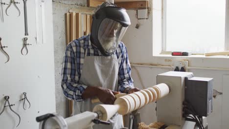 carpintero afroamericano de sexo masculino con casco protector girando madera en un torno en una carpintería